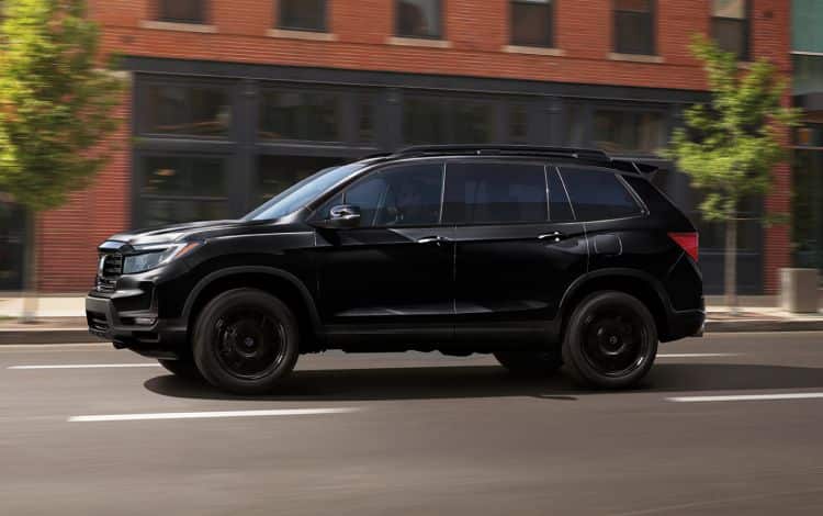 2024 Honda Passport Black Edition in Crystal Black Pearl, Profile at Urban brick building lined-road location, driving on a city street
