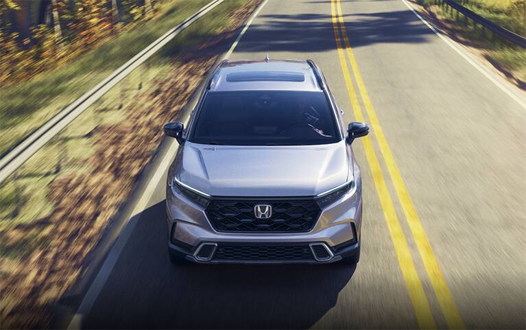 2027 Honda CR-V Sport Touring in Solar Silver Metallic top driving on a scenic winding forest road (Compact Crossover SUV).